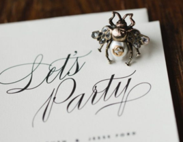 close-up of wedding invitation with metal bee trinket