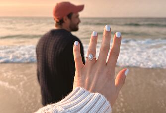 Close up image of engagement ring on hand with a man in the background