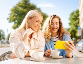 Best friends having coffee outside while smiling at a phone