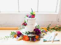 two tier buttercream wedding cake decorated with colorful purple, red and yellow flowers