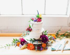 two tier buttercream wedding cake decorated with colorful purple, red and yellow flowers