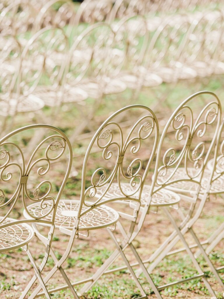 rows of white vintage wrought iron folding chairs on the grass at outdoor wedding ceremony