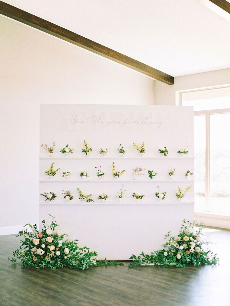 Modern escort card display with small flower pots and large arrangements underneat