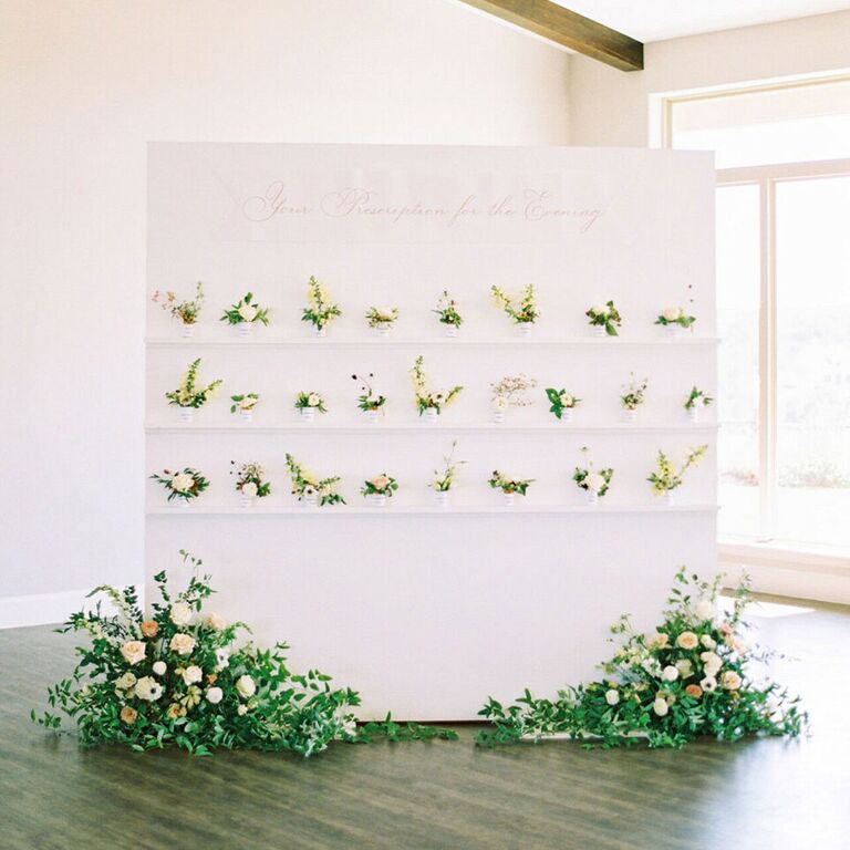 Modern escort card display with small flower pots and large arrangements underneat