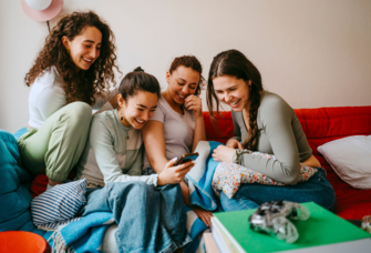 Group of women on couch looking at phone, best bachelorette party planning apps
