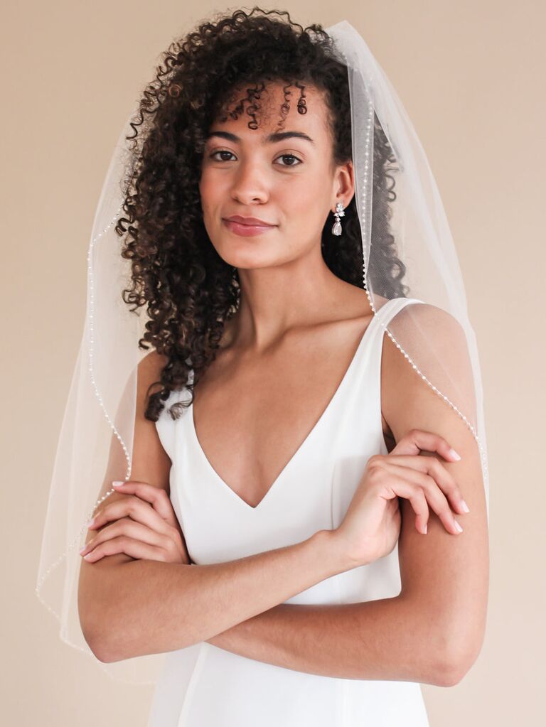 Model wears a mid-length veil with a pearl border. 