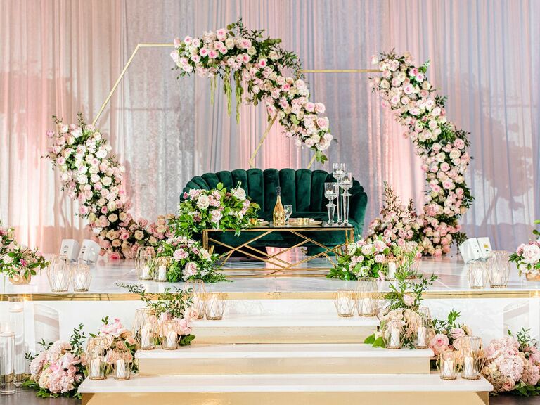 Sweetheart table on stage with emerald velvet couch and gold hexagon arch backdrop