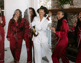 Bride wearing white pajamas and bridesmaids wearing matching red bridesmaid pajamas popping champagne