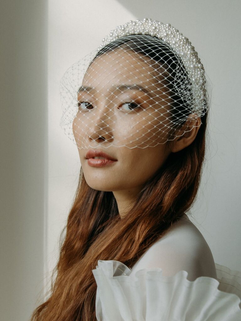 Model wears a birdcage veil attached to a pearl-crusted headband. 