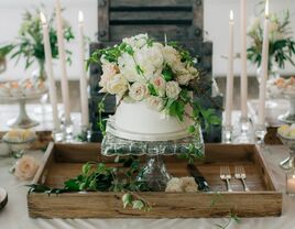 one tier wedding cake with ivory and blush flowers displayed atop glass cake stand