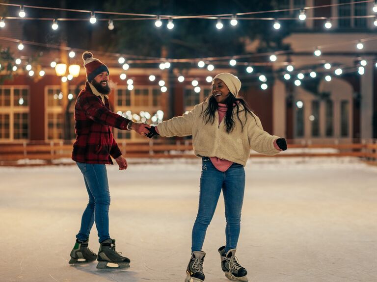 Couple ice skates while holding hands. 