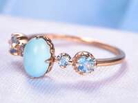 Cushion cut turquoise stone in center framed by blue topaz stones on rose gold band