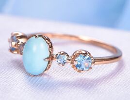 Cushion cut turquoise stone in center framed by blue topaz stones on rose gold band