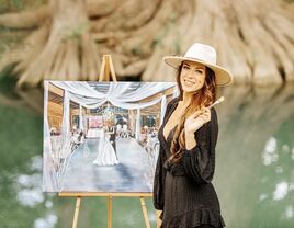 Artist holding up a paintbrush beside her beautiful wedding painting