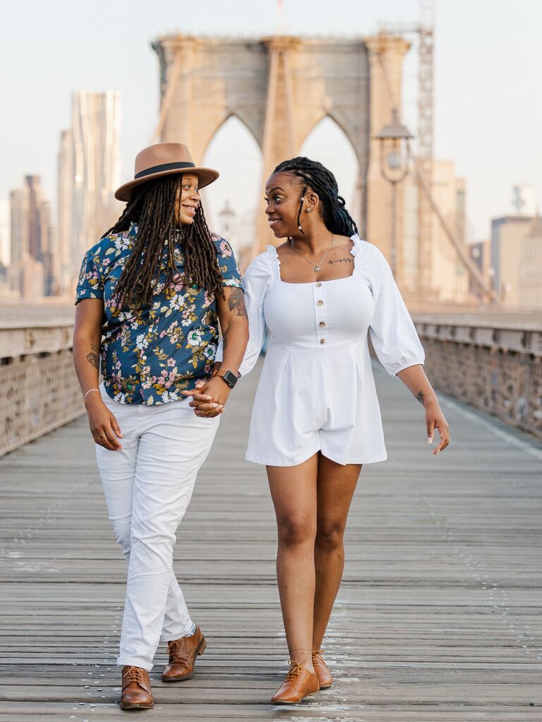 Couple smile and hold hands on the Brooklyn Bridge. 