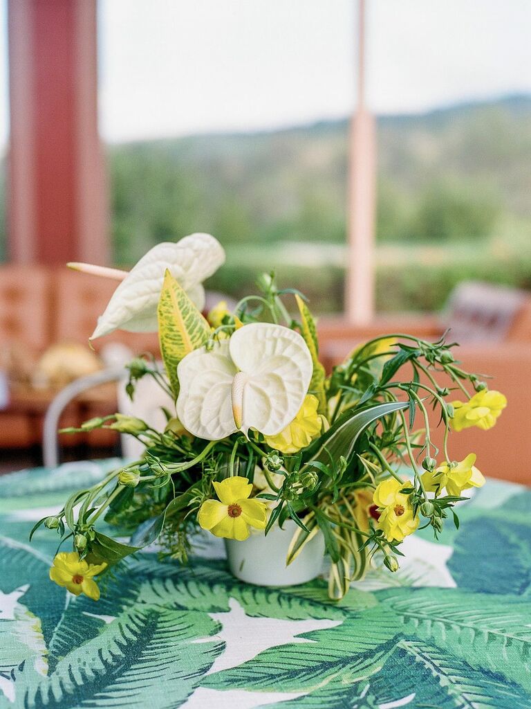 tropical small wedding centerpiece with white anthurium and yellow flowers on tablecloth with monstera leaf print 