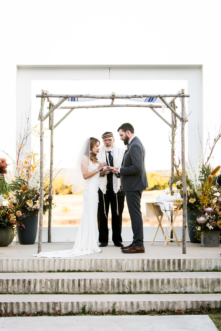 Couple exchanging rings under birch wood chuppah.