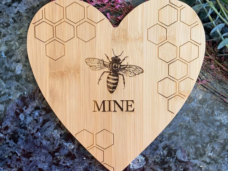 Heart shaped wooden cutting board with bee illustration and 'Mine' below it