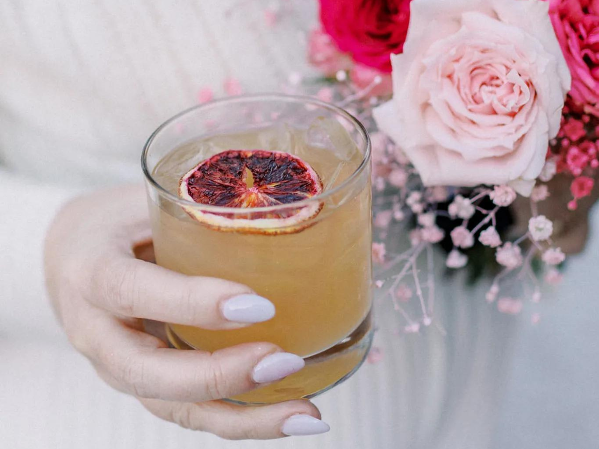 Bride holding orange wedding mocktail with bouquet