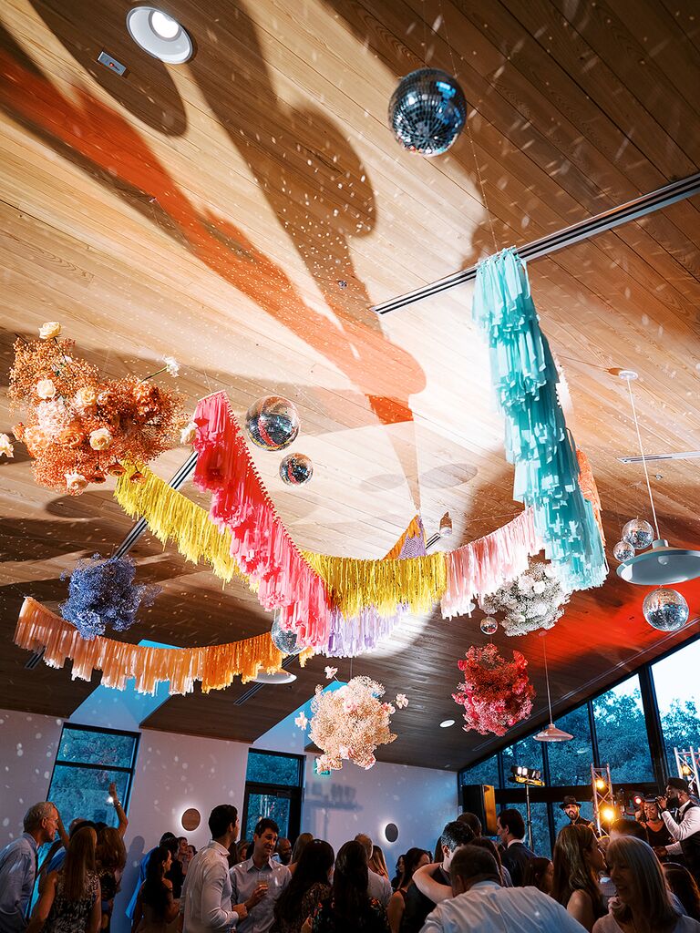 Guests enjoy a party beneath a rainbow of streamers and disco balls.