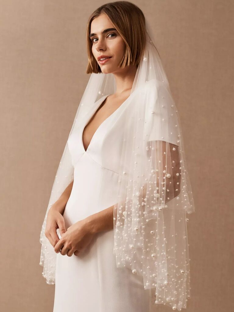 Model wears a retro mid-length veil with pearl embellishments. 