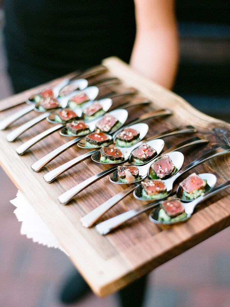 server holding wooden tray with seared tuna bites on metal spoons