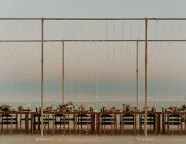 outdoor wedding venue with long banquet table surrounded by a curtain of string lights on both sides