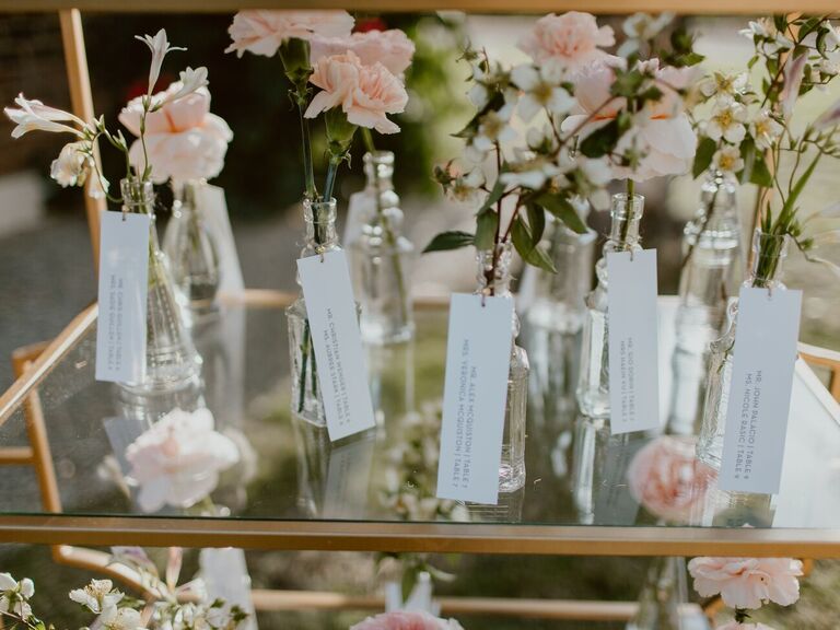 Escort cards attached to vintage bottles holding pink carnations