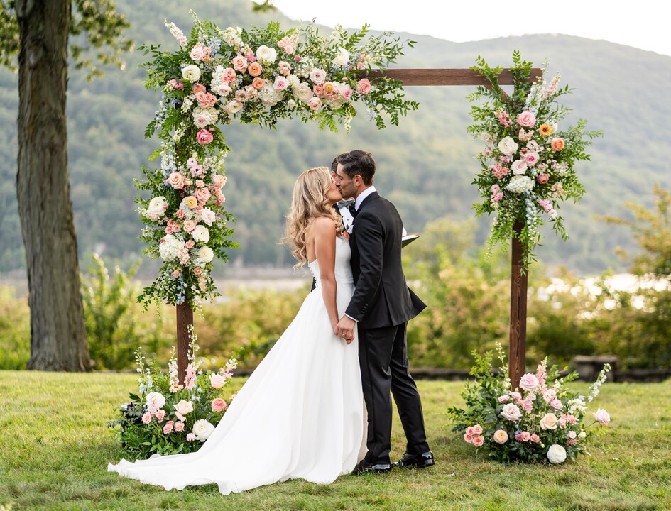 a bride and groom kissing under a frame of flowers and surrounded by nature - wedding vendors list