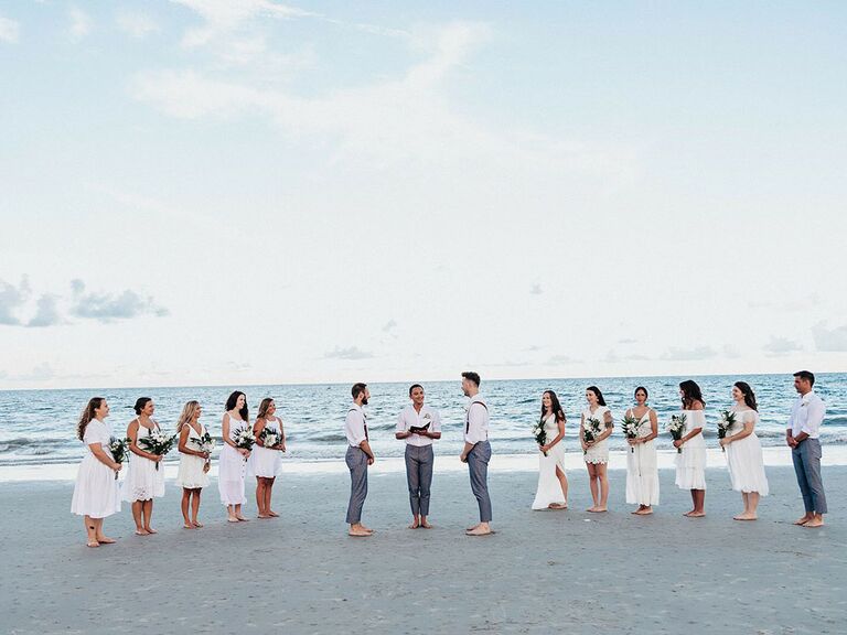 Grooms and wedding party in all-white outfits during oceanfront ceremony