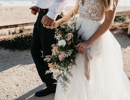 Bride holding wedding flower bouquet walking on beach with groom