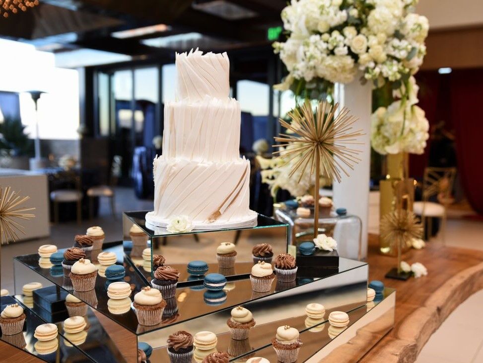 Three-tier white wedding cake with brown and blue cupcakes and macaroons