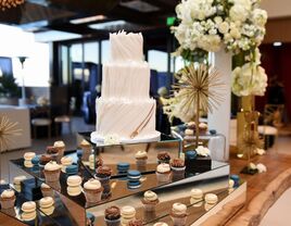Three-tier white wedding cake with brown and blue cupcakes and macaroons