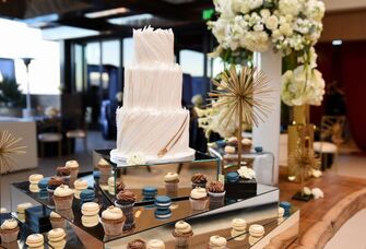 Three-tier white wedding cake with brown and blue cupcakes and macaroons