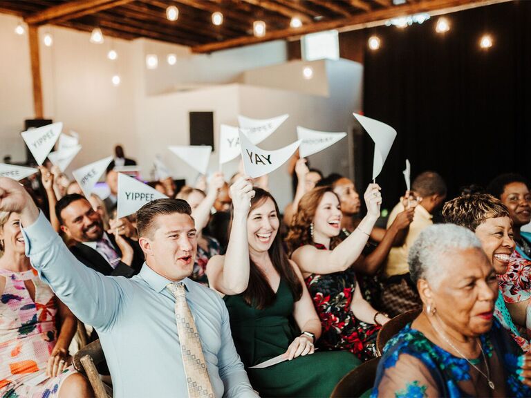Guests holding up flags that say "Yippee" and "Yay" at wedding ceremony