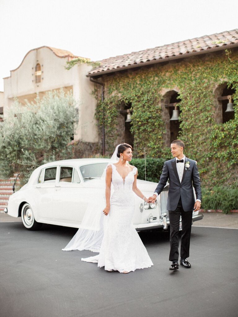 Bride and groom standing in front of getaway car