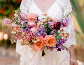Bride holding coral, lavender, and lilac mixed-floral bridal bouquet