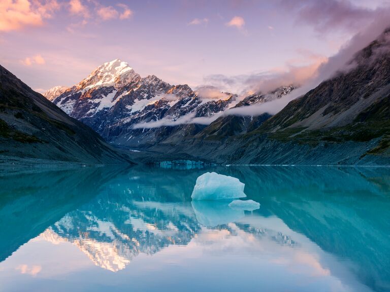 Snowcapped peak of mount Cook reflecting in still lake with iceberg at sunset in New Zealand