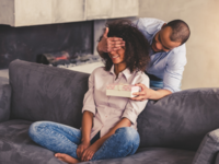 Man covering woman's eyes and surprising her with gift