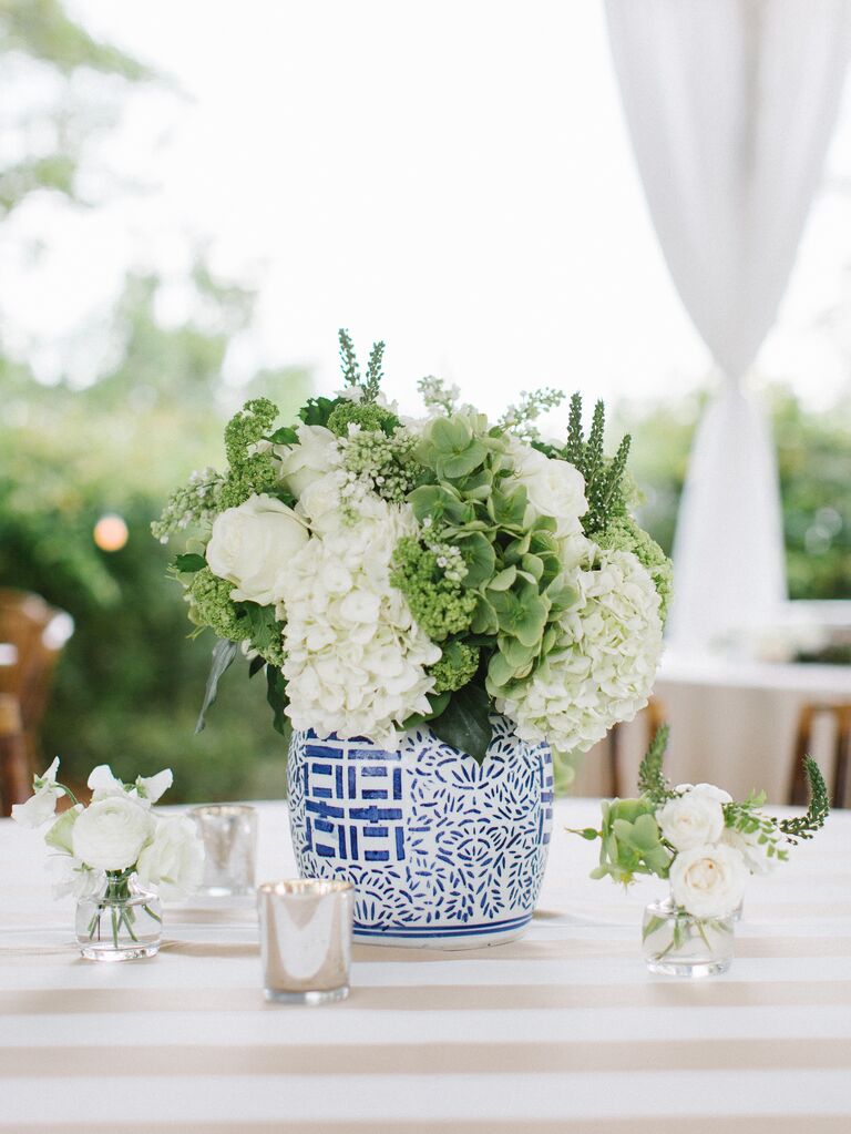 nautical wedding theme centerpiece with hydrangeas and greenery in blue chinoiserie vase on ivory and white striped tablecloth