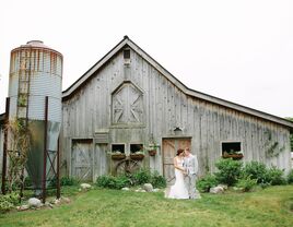 Bride and groom stand in front of a barn on their wedding day