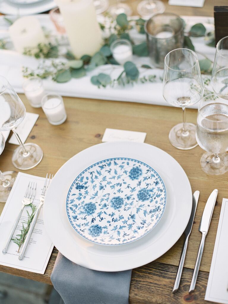 wedding place setting with blue floral print plate against bare wood table and light blue fabric napkin