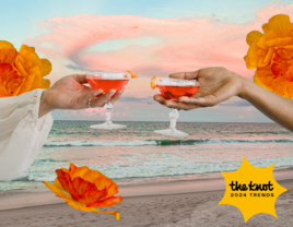 two women clicking glasses with beach backdrop and orange flowers