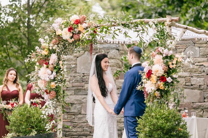 Couple holding hands under birch chuppah with dahlias accents.