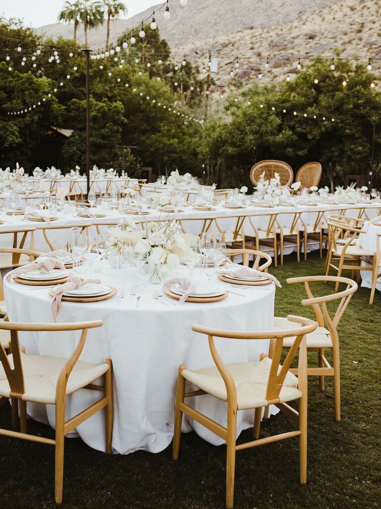 modern outdoor wedding reception with round banquet tables decorated in white linens and light wood wishbone chairs