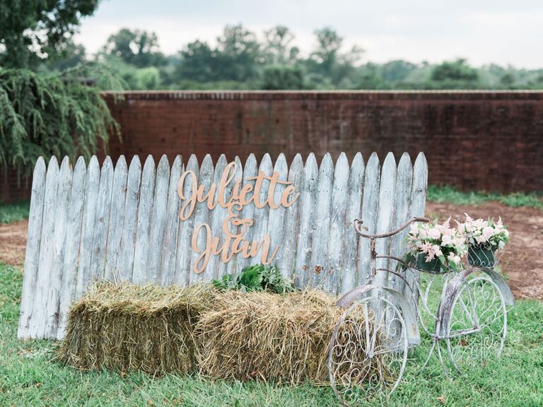 Shabby chic photobooth with distressed fence and hay bale next to vintage bike at barn wedding