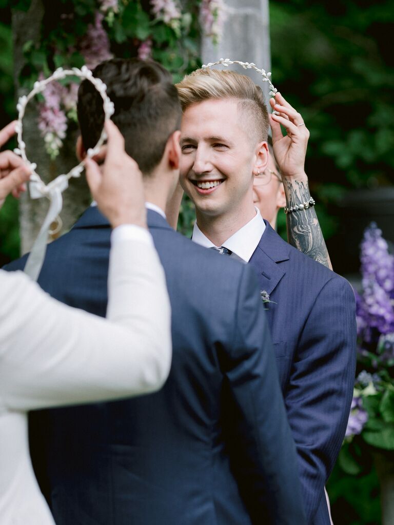 Grooms get stefana flower crowns placed on their heads during the wedding ceremony.