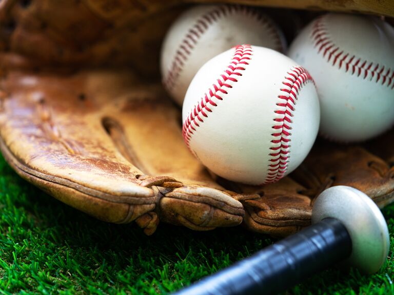 Three baseballs in a leather catcher's mitt beside the handle of a baseball bat.