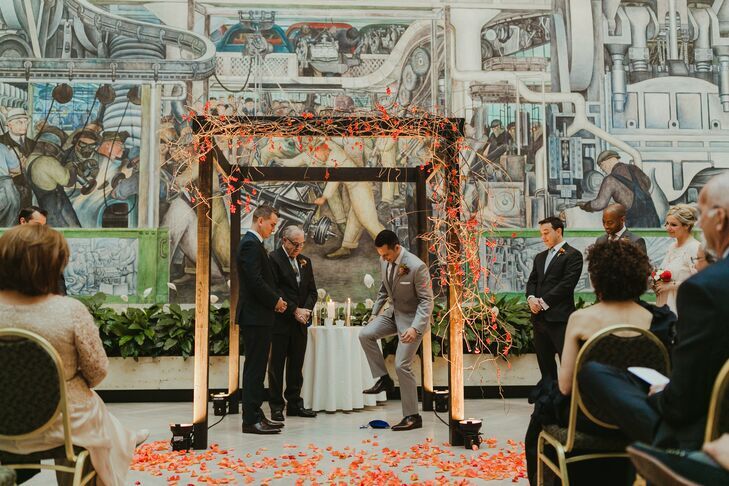 Groom breaking the glass under wood chuppah decorated with orange flowers. 