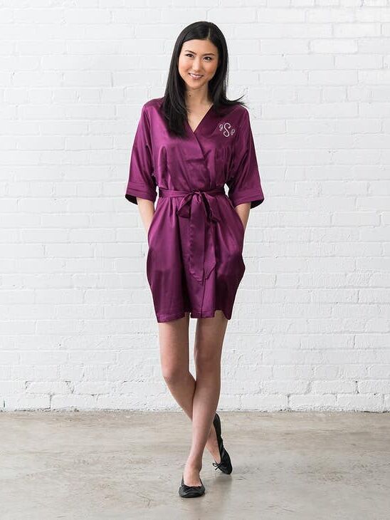 Model wearing a short satin robe in plum with an embroidered initials on the front